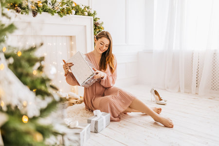 Beautiful cheerful happy young girl with christmas gifts on the background of a new year tree at homeの写真素材