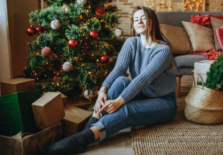 Beautiful cheerful happy young girl with christmas gifts on the floor near the new year tree at homeの写真素材