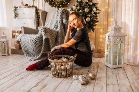 Beautiful cheerful happy young girl on the floor in pajamas with christmas toys near the new year tree at homeの写真素材