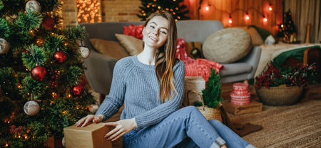 Beautiful cheerful happy young girl lays down christmas gifts on the floor near the new year tree at homeの写真素材