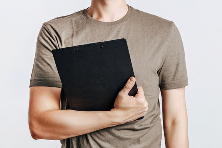 Young handsome man holding folder for papers with documents, student, worker looks data information, posing for photo isolated on gray background. Place for advertising.の写真素材