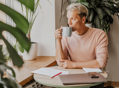 Man works in the workplace with documents and and drinks coffee in an eco cafe with plantsの写真素材