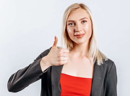 Smiling woman showing thumbs up and looking at the camera over white background. Positive girl shows like. OKの写真素材