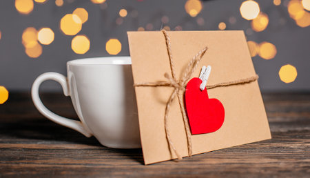Love letter with a heart next to a cup on a background of lights, love and valentine concept on a wooden tableの写真素材