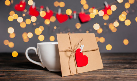 Love letter with a heart next to a cup on a background of lights, love and valentine concept on a wooden tableの写真素材