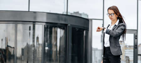 A business woman checks the time in the city during a working day waiting for a meeting. Discipline and timing. An employee goes towards a corporate meeting.の写真素材