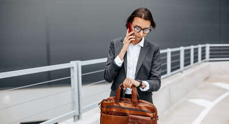 A business woman checks the time in the city during a working day waiting for a meeting. Discipline and timing. An employee goes towards a corporate meeting.の写真素材