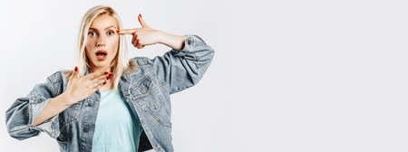 Beautiful young cute girl surprised and showing gun gesture on gray isolated backgroundの写真素材