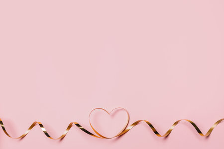 shape heart by gold ribbon on isolated pink backgroundの写真素材