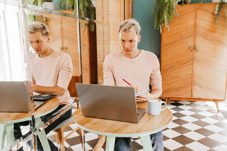 Happy business man sitting at cafeteria with laptop and smartphone. Businessman texting on smart phone while sitting in a cafe, working and checking email on computerの写真素材