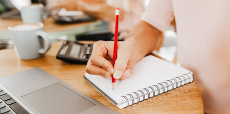 Man writes business information in notebook at workplace in office with calculator and laptopの写真素材