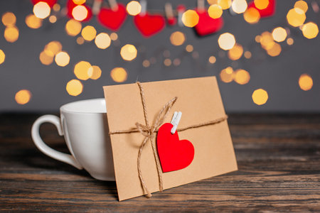 Love letter with a heart next to a cup on a background of lights, love and valentine concept on a wooden tableの写真素材