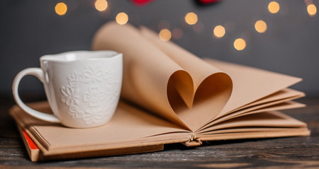 Heart made from book sheets with a cup, love and valentine concept on a wooden tableの写真素材