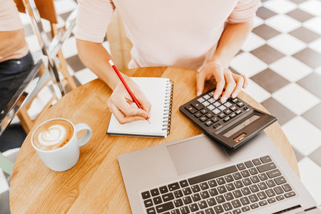 Man writes business information in notebook at workplace in office with calculator and laptopの写真素材