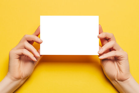 Female hands hold a blank sheet of paper on a yellow background. Advertising spaceの写真素材