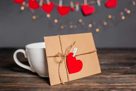 Love letter with a heart next to a cup on a background of lights, love and valentine concept on a wooden tableの写真素材