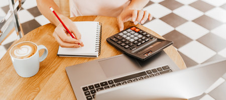 Man writes business information in notebook at workplace in office with calculator and laptopの写真素材