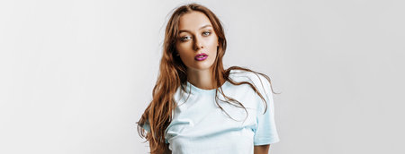 Beautiful young brunette girl with green eyes with long hair with fashion makeup with purple lips on an isolated gray background. The woman seriously looking at the camera. Kind cute modelの写真素材