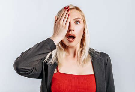 The blonde girl is surprised badly covers half of her face with her hand. The woman remembered, learned and understood important information about the business. Isolated background for advertising.の写真素材