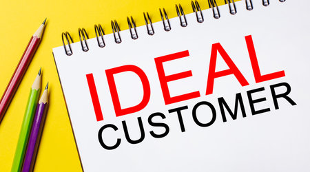 IDEAL CUSTOMER on a white notepad with pencils on a yellow background. Business conceptの写真素材