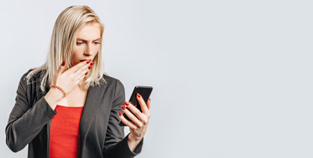 Beautiful young girl unhappy and holding phone on gray isolated backgroundの写真素材