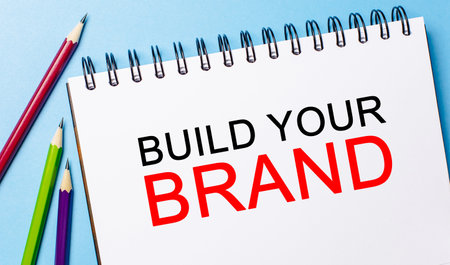 Text Build Your Brand on a white notepad with pencils on a blue background. Business conceptの写真素材
