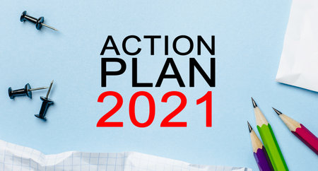 Text ACTION PLAN 2021 on a white notepad with pencils on a blue background. Business conceptの写真素材