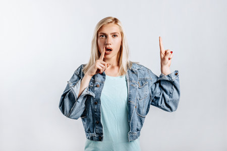 Look here. Young beautiful blonde woman points her fingers to the top thinks and makes a decision. The woman thought about the choice. Place for advertising.の写真素材