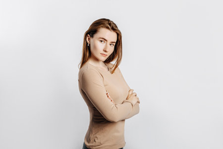 Beautiful young girl smiling and posing looking at the camera on a white isolated background. Positive brunette woman in a beige jumper. Kind look.の写真素材