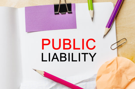 Text PUBLIC LIABILITY on a white notepad with pencils on a wooden background. Business conceptの写真素材