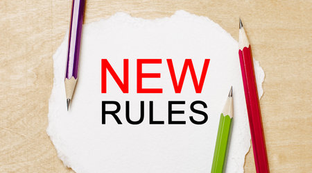 Text new rules on a white notepad with pencils on a wooden background. Business conceptの写真素材