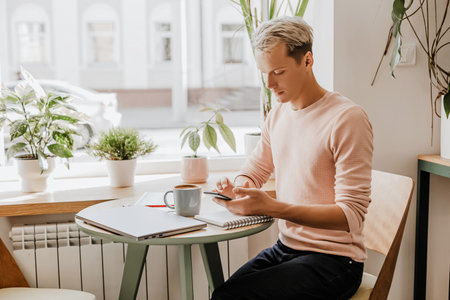 Man works in the workplace with documents and and drinks coffee in an eco cafe with plantsの写真素材