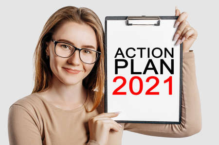 ACTION PLAN 2021. Beautiful young business woman wearing glasses holds a clipboard with mock up...