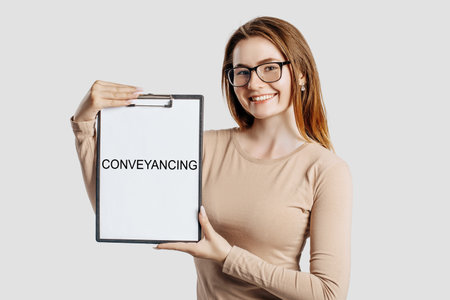 Conveyancing. Beautiful young business woman wearing glasses holds a clipboard with mock up space isolated on gray backgroundの写真素材