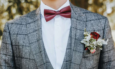 Groom in a suit with a wedding flower boutonniere and a red bow tie in natureの写真素材