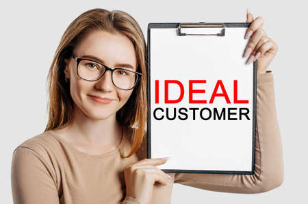 IDEAL CUSTOMER. Beautiful young business woman wearing glasses holds a clipboard with mock up space isolated on gray backgroundの写真素材