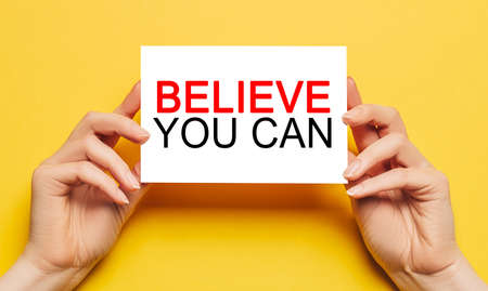 Female hands hold card paper with text Believe you can on a yellow background. Business and finance conceptの写真素材