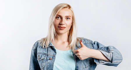Smiling woman showing thumbs up and looking at the camera over white background. Positive girl shows like. OKの写真素材