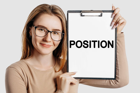 POSITION. Beautiful young business woman wearing glasses holds a clipboard with mock up space isolated on gray backgroundの写真素材