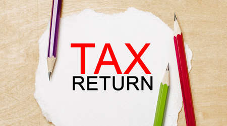 Text Tax return on a white notepad with pencils on a blue background. Business conceptの写真素材