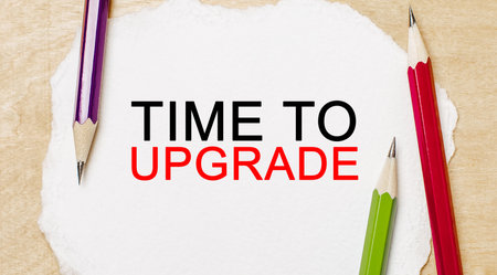 Text Time to upgrade on a white notepad with pencils on a wooden background. Business conceptの写真素材