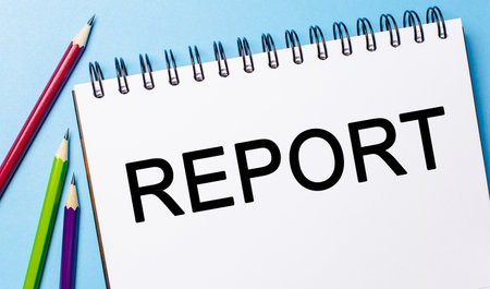 Text REPORT on a white notepad with pencils on a blue background. Business conceptの写真素材