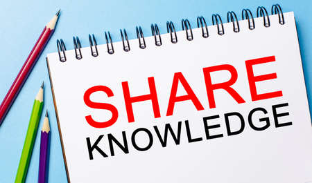 Text SHARE KNOWLEDGE on a white notepad with pencils on a blue background. Business conceptの写真素材