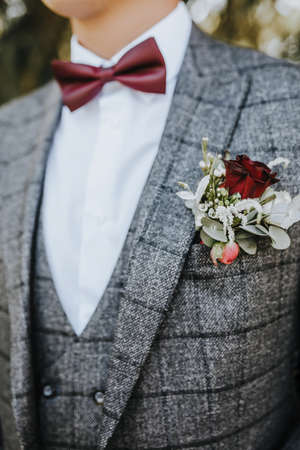 Groom in a suit with a wedding flower boutonniere and a red bow tie in natureの写真素材