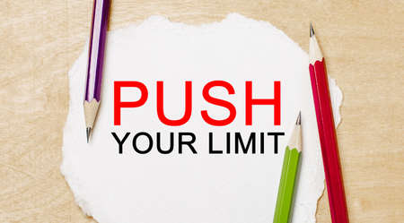 Text PUSH YOUR LIMIT on a white notepad with pencils on a wooden background. Business conceptの写真素材