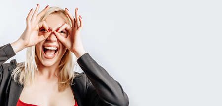 Beautiful young cute girl smiling fooling around and doing ok eye gesture on gray isolated backgroundの写真素材