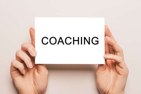 Female hands hold card paper with text COACHING on a yellow background. Business and finance conceptの写真素材