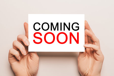 Female hands hold card paper with text COMING SOON on a yellow background. Business and finance conceptの写真素材