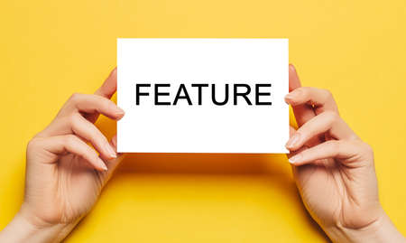 Female hands hold card paper with text FEATURE on a yellow background. Business and finance conceptの写真素材