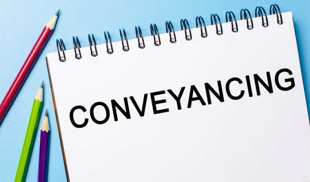 Text Conveyancing on a white notepad with pencils on a blue background. Business conceptの写真素材